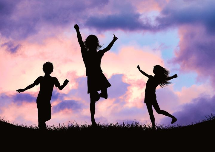 Three silhouetted children playing against a sky of peach and purple clouds.